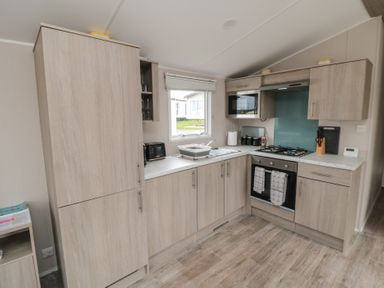 A kitchen with wooden cabinets a gas stove oven microwave and a window at Meadow View in West Thirston Felton
