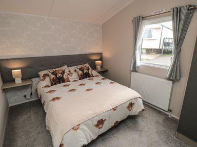 A bedroom with a double bed featuring animal print bedding two bedside tables with lamps a window with checked curtains and a radiator at Meadow View in West Thirston Felton