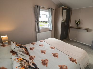 A bedroom with a bed with animal print bedding a window with checkered curtains a wardrobe and a wall shelf with flowers at Meadow View in West Thirston Felton