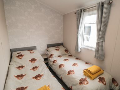 A bedroom with two single beds with animal print bedding and a window with checkered curtains at Meadow View in West Thirston Felton