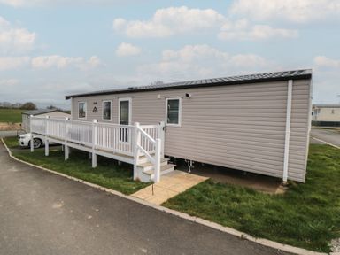 A beige mobile home with a white ramp and stairs on a grassy area next to a paved road at Meadow View in West Thirston Felton