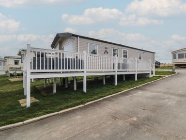 A mobile home with a white railing deck on a grassy plot next to a paved road at Meadow View in West Thirston Felton