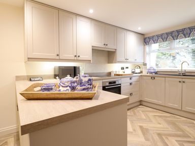 A kitchen with beige cabinets a wooden countertop a tea set on a tray and a window with a patterned valance at 6 Uppergate Street Rose Cottage in Conwy