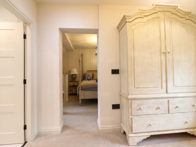 A hallway leading to a bedroom with a wooden bed and nightstand and a large wooden wardrobe in the foreground at 6 Uppergate Street Rose Cottage in Conwy