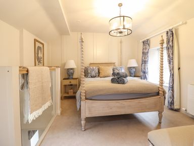 A bedroom with a carved four-poster bed with rolled towels bedside tables with lamps and patterned curtains at 6 Uppergate Street Rose Cottage in Conwy