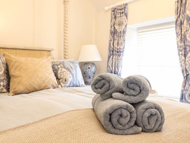 A bedroom with a bed pillows a lamp and rolled grey towels on the bed at 6 Uppergate Street Rose Cottage in Conwy