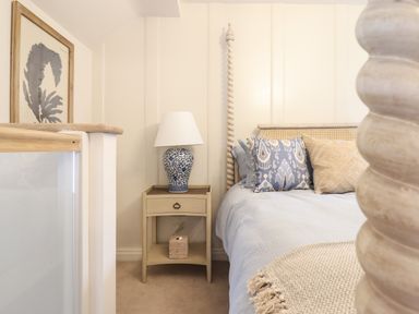A bedroom with a bed a nightstand with a lamp and framed artwork at 6 Uppergate Street Rose Cottage in Conwy