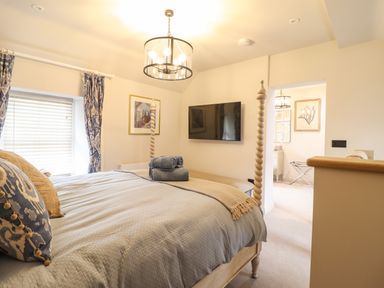 A bedroom with a bed stacked towels a wall-mounted TV curtains and a light fixture at 6 Uppergate Street Rose Cottage in Conwy
