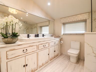 A bathroom with a large mirror white double sink vanity a toilet and window blinds at 6 Uppergate Street Rose Cottage in Conwy