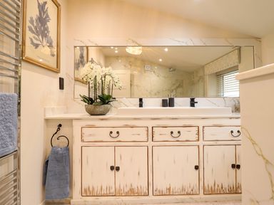 A bathroom vanity with a sink cabinet a large mirror a towel hanging and a plant on the countertop at 6 Uppergate Street Rose Cottage in Conwy