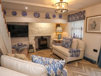 A sitting room with cream sofas blue patterned cushions a stone fireplace and a wall-mounted television at 6 Uppergate Street Rose Cottage in Conwy