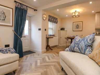 A living room with beige sofas blue patterned cushions a dining table with chairs and framed artwork at 6 Uppergate Street Rose Cottage in Conwy
