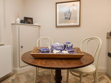 A wooden round table with a tray holding blue and white tea set and two white chairs in a dining area at 6 Uppergate Street Rose Cottage in Conwy