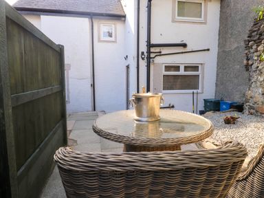 A small outdoor patio with a round glass table and wicker chairs next to a white house at 6 Uppergate Street Rose Cottage in Conwy