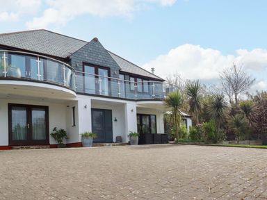 The exterior of a two story house with a paved driveway and glass balcony at Goatsland in Trebetherick