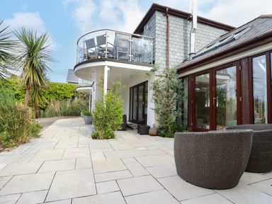 Outdoor patio area with wicker chairs plants and balconies with glass railings at Goatsland in Trebetherick