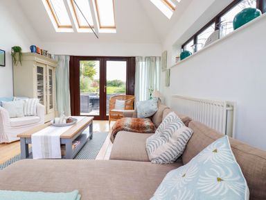 A living room with a sofa and armchair around a coffee table under skylights at Goatsland in Trebetherick