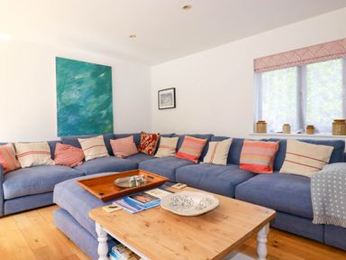 A living room with a blue sectional sofa with throw pillows and a wooden coffee table at Goatsland in Trebetherick