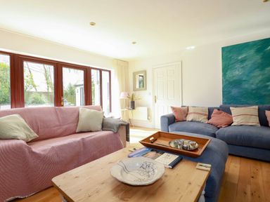 A living room with two sofas a wooden coffee table and large glass doors at Goatsland in Trebetherick