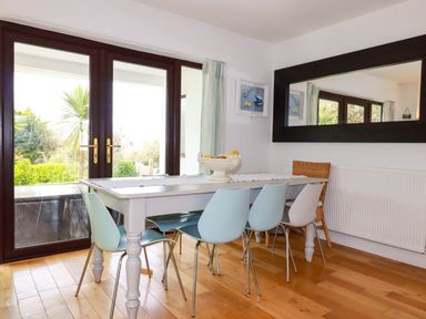 A dining room with a white table and blue chairs next to glass doors at Goatsland in Trebetherick