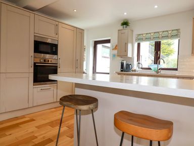 A kitchen with beige cabinets a countertop bar with two wooden stools and a window at Goatsland in Trebetherick