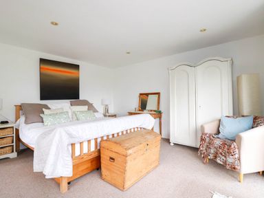 A bedroom with a wooden bed and chest a white wardrobe a chair with a blanket and a lamp at Goatsland in Trebetherick
