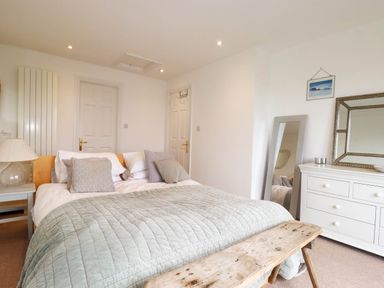 A bedroom with a bed pillows lamps bedside table bench mirror and dresser at Goatsland in Trebetherick