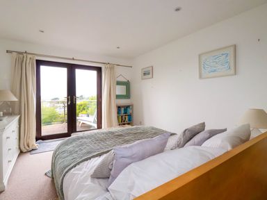 A bedroom with a bed facing glass doors leading to a balcony at Goatsland in Trebetherick