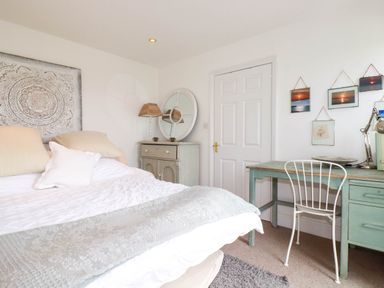 A bedroom with a bed a bedside cabinet a desk with a chair and wall art at Goatsland in Trebetherick
