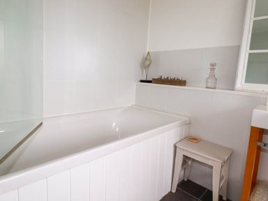 A bathroom with a white bathtub and a stool next to it at Goatsland in Trebetherick