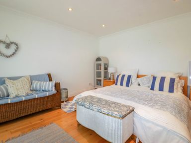 A bedroom with a bed a cushioned wicker bench a wicker sofa and a cabinet at Goatsland in Trebetherick