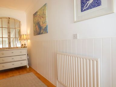 A corner of a room with a white radiator a chest of drawers a lamp and two paintings on the wall at Goatsland in Trebetherick