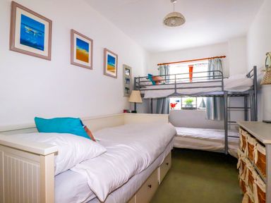 A bedroom with a bunk bed and a single bed with pillows a lamp and framed pictures on the wall at Goatsland in Trebetherick