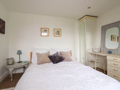 A bedroom with a bed cushions a bedside table a lamp a wardrobe and a dresser with a mirror at Goatsland in Trebetherick