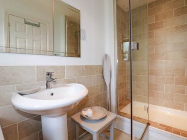A bathroom with a pedestal sink a mirror a small stool with a bowl and towel a wooden paddle and a walk-in shower at Goatsland in Trebetherick