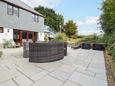 A paved patio with outdoor furniture and a garden with trees behind at Goatsland in Trebetherick