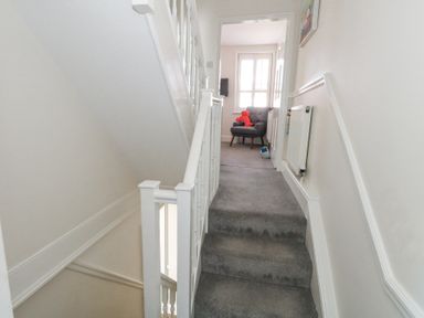 A carpeted staircase leading to a hallway with a chair holding a red stuffed toy at Shrimp Cottage in Brewers Quay Harbour