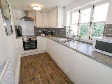 A narrow kitchen with wooden floor white cabinets a sink microwave oven and window at Shrimp Cottage in Brewers Quay Harbour