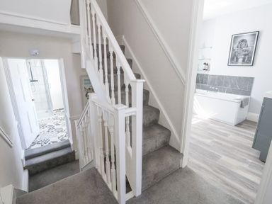 A stairway with grey carpet leading down to a bathroom with patterned floor tiles and another bathroom with wood flooring and a bathtub at Shrimp Cottage in Brewers Quay Harbour
