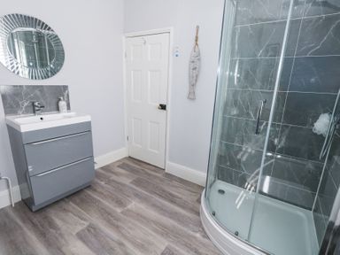 A bathroom with a shower enclosure a sink with cabinet and a round mirror at Shrimp Cottage in Brewers Quay Harbour
