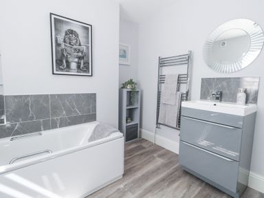 A bathroom with a bathtub a vanity with a sink a round mirror a towel rack and a framed picture at Shrimp Cottage in Brewers Quay Harbour