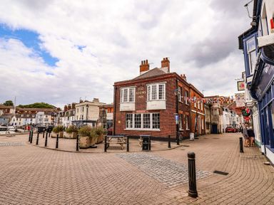 A brick building with the sign Old Rooms Inn at a street corner near boats and other buildings at Brewers Quay Harbour