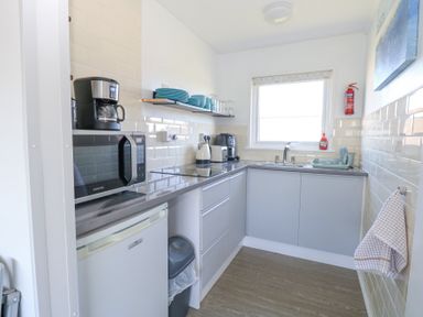 A small kitchen with grey cabinets a microwave coffee maker kettle and dishes on a shelf at Chalet 37 in Hemsby