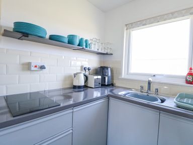 A kitchen counter with a sink toaster kettle air fryer and blue dishes on a shelf at Chalet 37 in Hemsby
