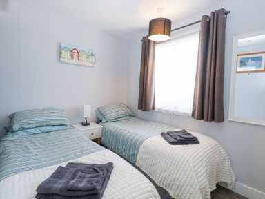 A bedroom with two single beds a nightstand with a lamp and a window with curtains at Chalet 37 in Hemsby