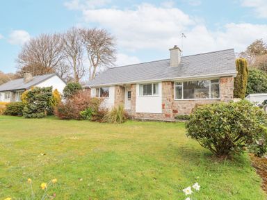 A front view of a stone and white house with a lawn and bushes at 3 Glyn Y Mor in Llanbedrog