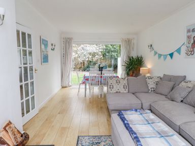 A living room with a gray sectional sofa and a dining table with white chairs near a sliding glass door at 3 Glyn Y Mor in Llanbedrog