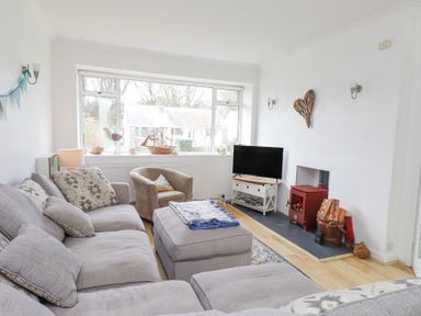 A living room with a sectional sofa an armchair a wood stove and a television at 3 Glyn Y Mor in Llanbedrog