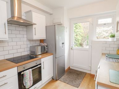 A kitchen with white cabinets a stainless steel oven and range hood a microwave on the counter and a refrigerator next to a door with a window at 3 Glyn Y Mor in Llanbedrog
