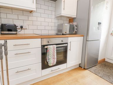 A kitchen with white cabinets a built in oven a microwave a toaster and a refrigerator at 3 Glyn Y Mor in Llanbedrog